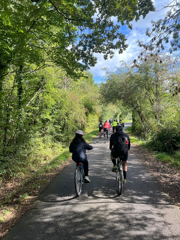 Cyclists are seen riding on a narrow road on what looks like a country lane.